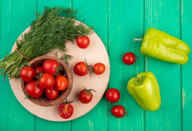 Top view of vegetables as bowl of tomatoes and bunch of dill on cutting board with peppers on green surface