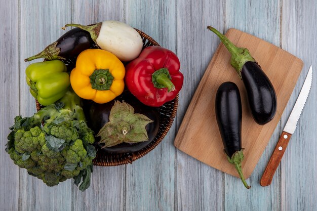 Top view of vegetables as broccoli  pepper and eggplant in basket and eggplants on cutting board with knife on wooden background