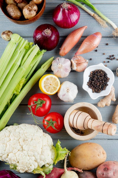 Top view of vegetables as celery onion tomato cauliflower and others with cut lemon and garlic crusher on wooden background