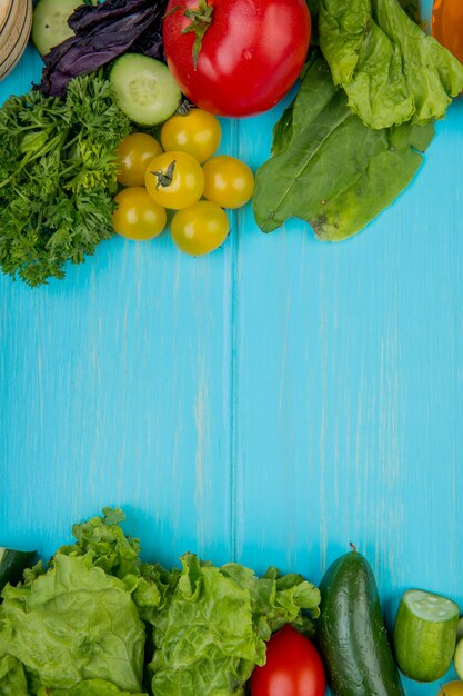 Top view of vegetables as coriander basil tomato spinach lettuce cucumber on blue surface with copy space