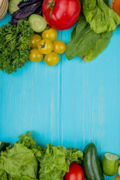 Top view of vegetables as coriander basil tomato spinach lettuce cucumber on blue with copy space