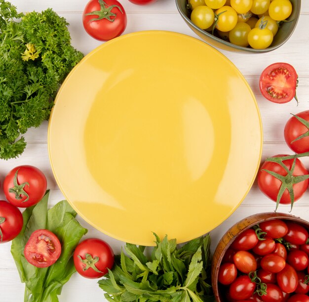 Top view of vegetables as coriander tomato spinach green mint leaves with empty plate on center on wood