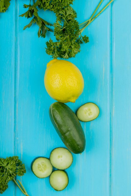 Top view of vegetables as cucumber coriander with lemon on blue surface