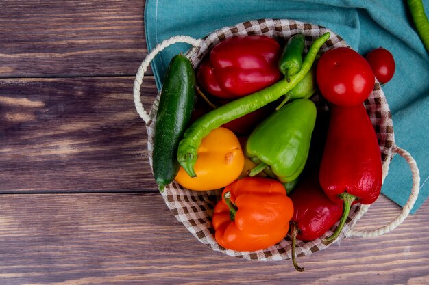 Top view of vegetables as cucumber pepper tomato in basket on blue cloth and wooden surface with copy space