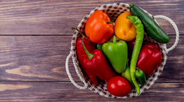 Top view of vegetables as cucumber pepper tomato in basket on wooden surface with copy space