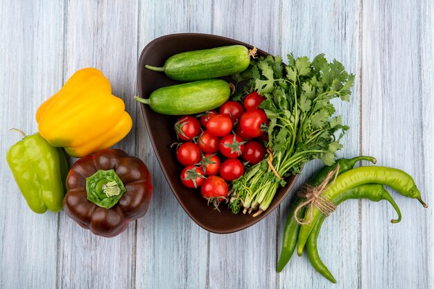 Top view of vegetables as cucumber tomato bunch of coriander in bowl with peppers on wooden surface