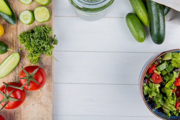 Top view of vegetables as cucumber tomato coriander on cutting board and cucumbers in sack with vegetable salad on wood with copy space