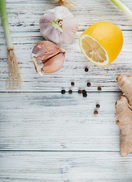 Top view of vegetables as garlic lemon ginger scallion with black pepper grains on wooden background with copy space