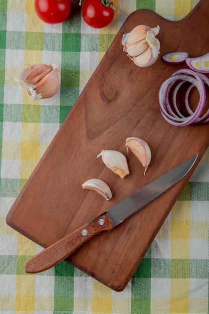 Top view of vegetables as garlic onion tomato with cutting board and knife on cloth surface