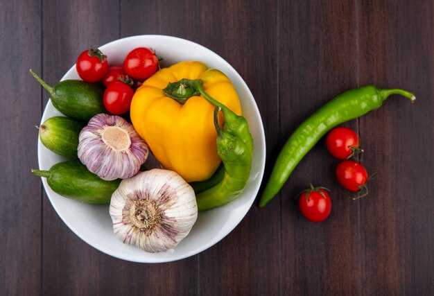 木の表面にニンニクピーマンキュウリとトマトのボウルとして野菜のトップビュー