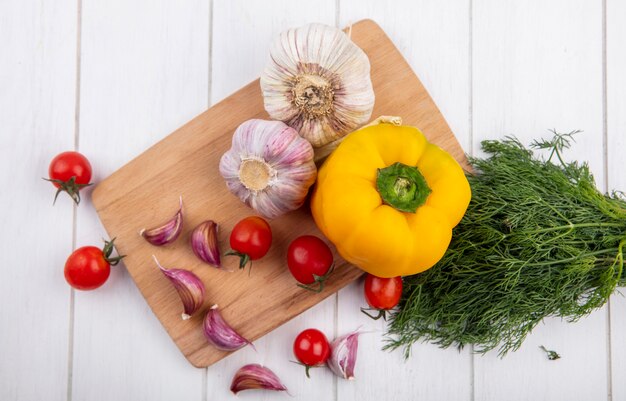 Top view of vegetables as garlic tomato pepper on cutting board with dill on wooden surface