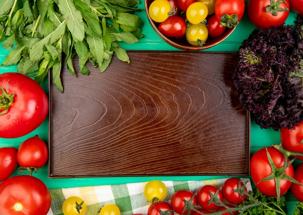 Top view of vegetables as green mint leaves basil tomato around empty tray on green surface