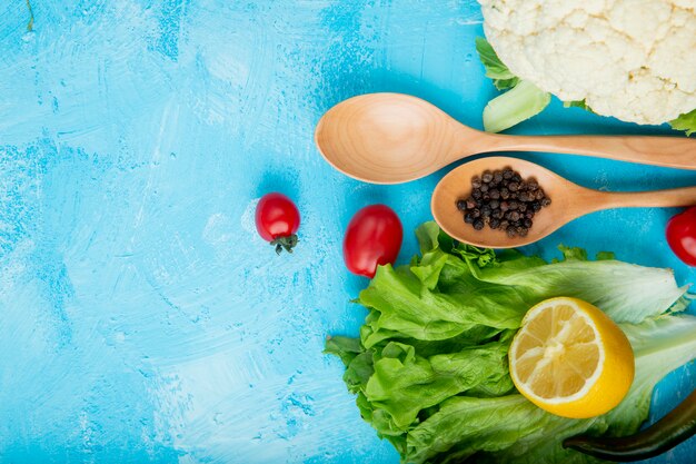 Top view of vegetables as lettuce, tomato, cauliflower with lemon and pepper spice on blue surface