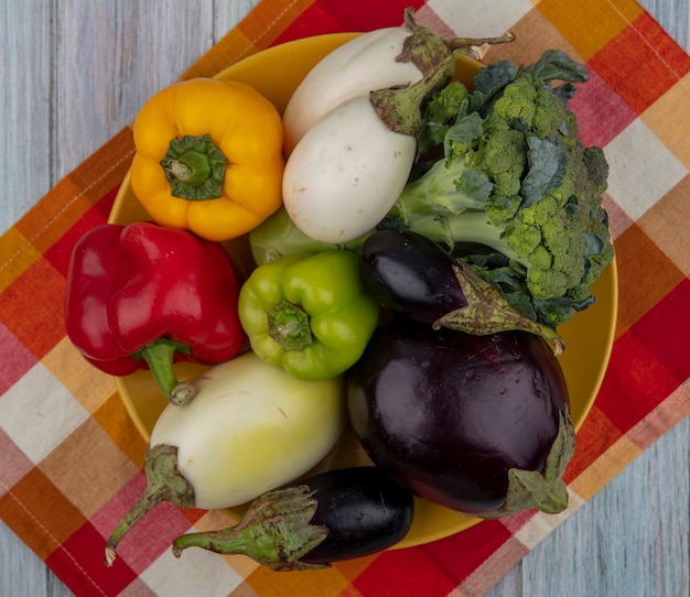 Free photo top view of vegetables as pepper  broccoli and eggplant in plate on plaid cloth on wooden background