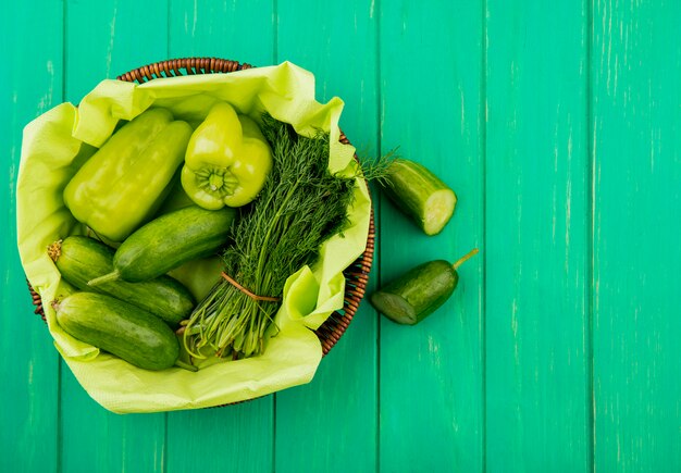 Top view of vegetables as pepper cucumber dill in basket with cut cucumber on green surface