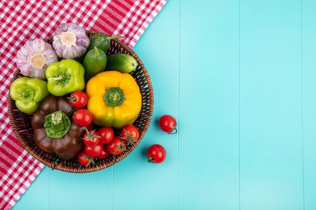 Top view of vegetables as pepper cucumber garlic tomato in basket on plaid cloth and blue surface