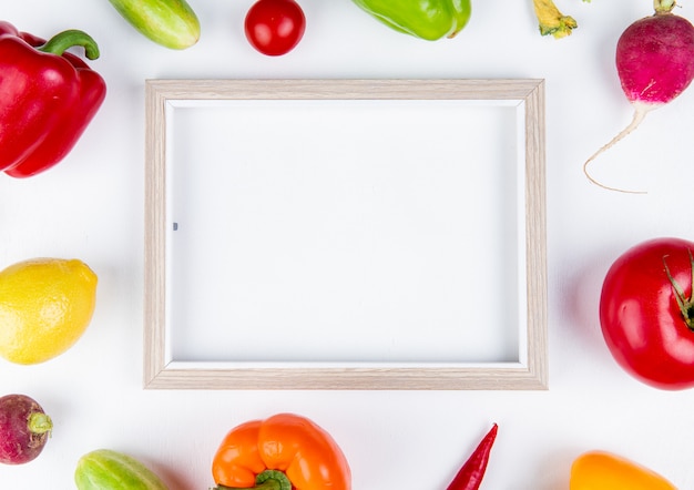 Top view of vegetables as pepper cucumber radish tomato with frame on white surface with copy space