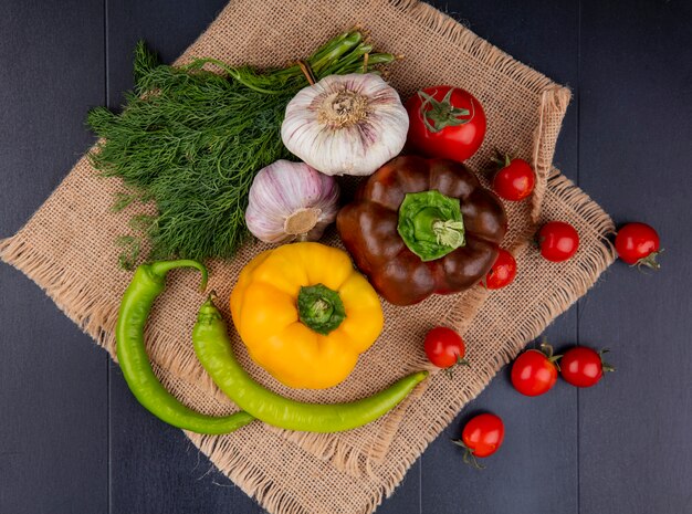 Top view of vegetables as pepper garlic dill tomato on sackcloth on black surface