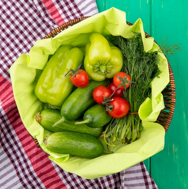 格子縞の布と緑の表面にバスケットのペッパートマトキュウリディルとして野菜のトップビュー