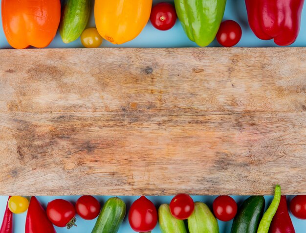 Top view of vegetables as pepper tomato cucumber with cutting board on blue surface