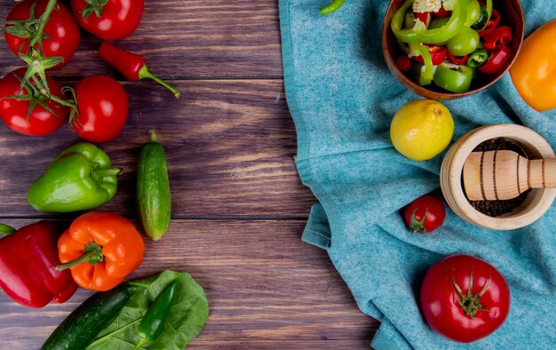 Top view of vegetables as pepper tomato with garlic crusher and lemon on blue cloth and cucumber tomato pepper leave on wood