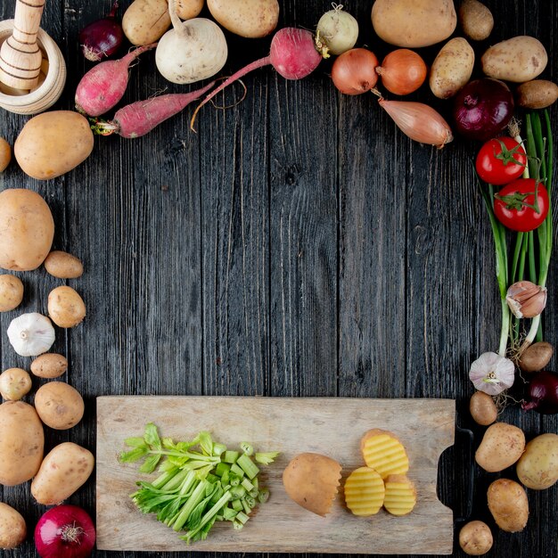 Top view of vegetables as scallion radish onion garlic with cut celery and potato on cutting board on wooden background with copy space