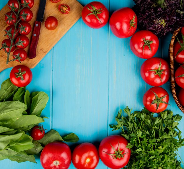 Top view of vegetables as spinach basil tomato coriander with knife on cutting board on blue surface with copy space