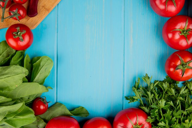 복사 공간이 파란색 표면에 커팅 보드에 칼으로 시금치 토마토 고수로 야채의 상위 뷰