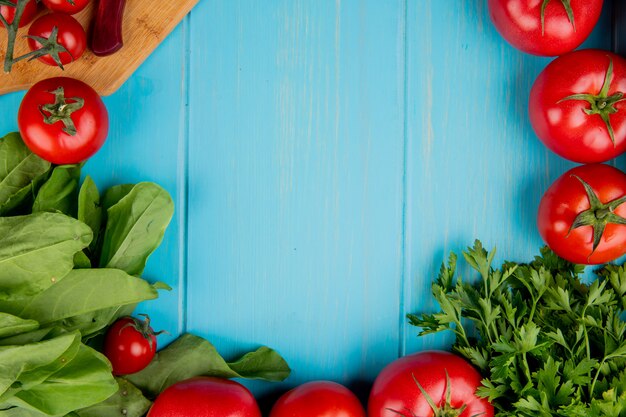 Top view of vegetables as spinach tomato coriander with knife on cutting board on blue with copy space