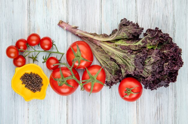 Top view of vegetables as tomato basil with bowl of black pepper seeds on wooden surface