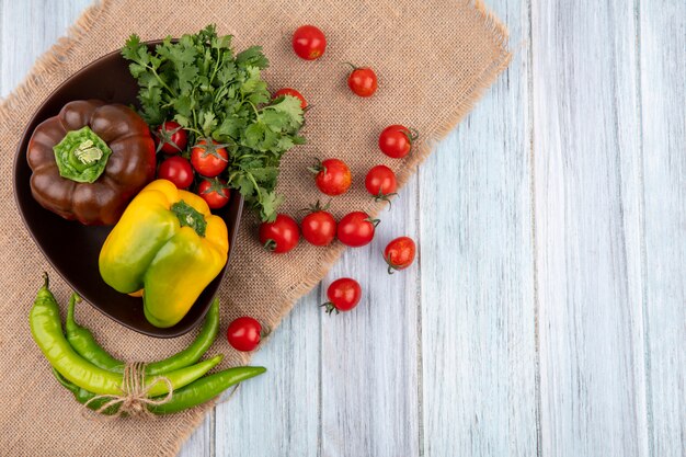 Top view of vegetables as tomato bunch of coriander pepper in bowl and on sackcloth on wooden surface