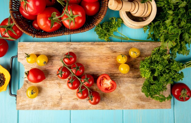 Top view of vegetables as tomato coriander on cutting board with garlic crusher black pepper on blue surface