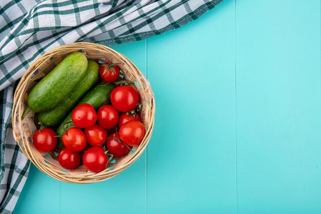 青い表面の格子縞の布の上のバスケットにトマトキュウリとして野菜のトップビュー