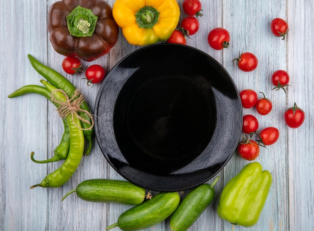 Foto gratuita vista superiore delle verdure come pepe del cetriolo del pomodoro intorno al piatto vuoto su superficie di legno