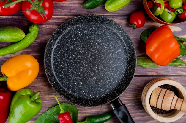 Top view of vegetables as tomato cucumber pepper with leaves and black pepper in garlic crusher and frying pan on wood