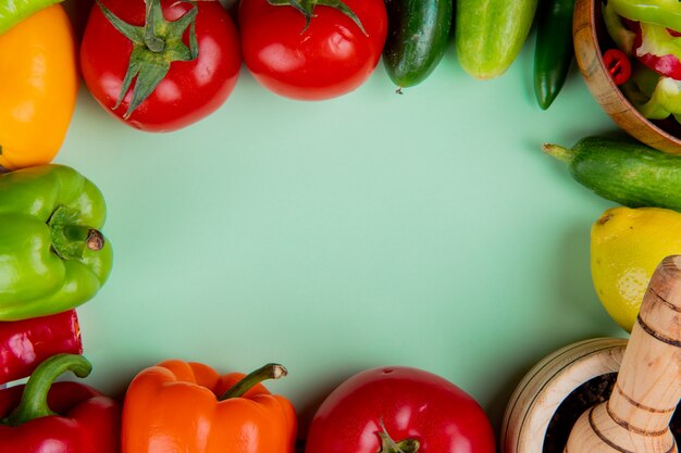 Top view of vegetables as tomato cucumber pepper with lemon and black pepper in garlic crusher on green surface with copy space