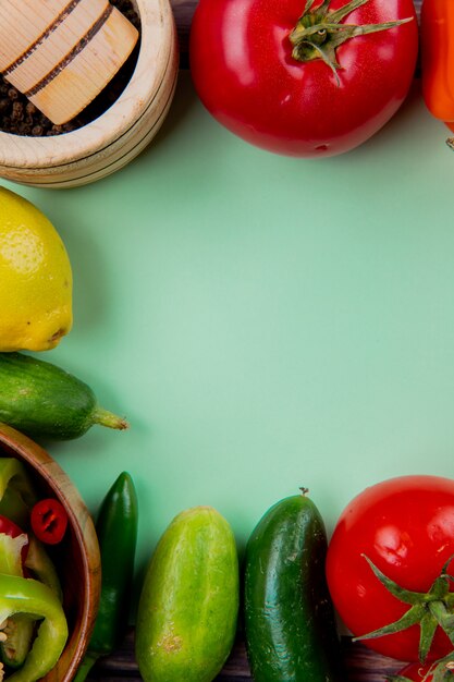 Top view of vegetables as tomato cucumber pepper with lemon and black pepper in garlic crusher on green surface with copy space