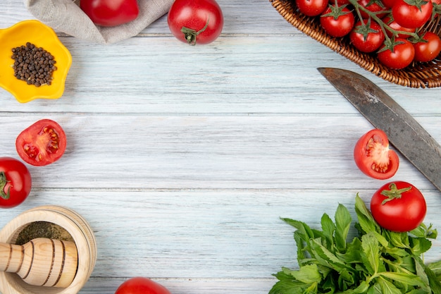 Top view of vegetables as tomato green mint leaves with black pepper garlic crusher and knife on wooden surface with copy space