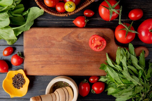 Top view of vegetables as tomato and green mint leaves with black pepper seeds and garlic crusher and cut tomato on cutting board on wood