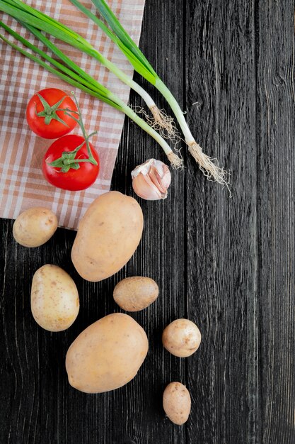 Top view of vegetables as tomato potato scallion and garlic on wooden background with copy space