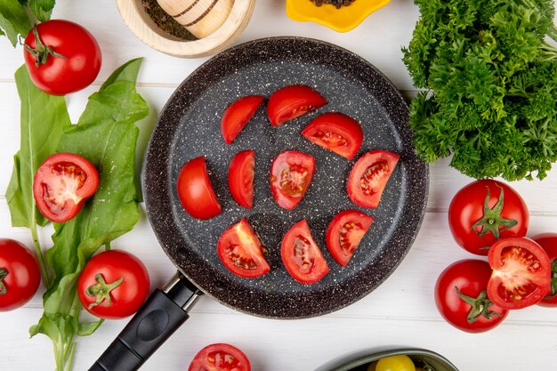 Top view of vegetables as tomato spinach coriander with tomato slices in frying pan on wooden surface