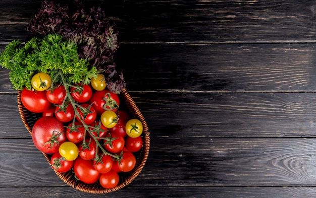 Top view of vegetables as tomatoes coriander basil in basket on wooden surface with copy space