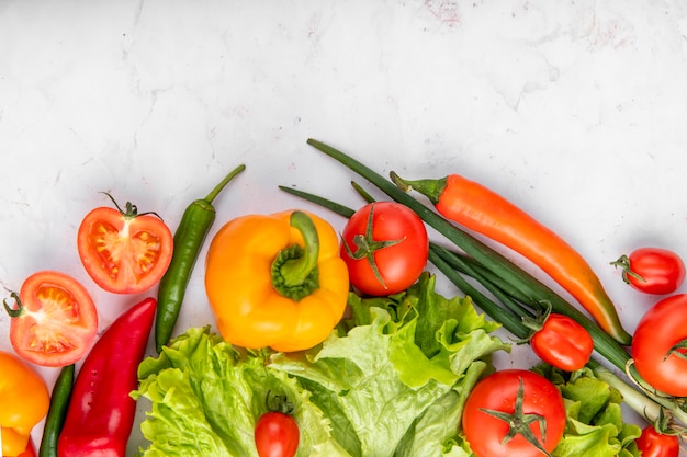 Top view of vegetables as tomatoes peppers broccoli and scallions on white surface