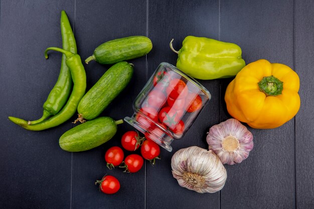 Top view of vegetables as tomatoes spilling out of jar garlic cucumber and pepper on black surface