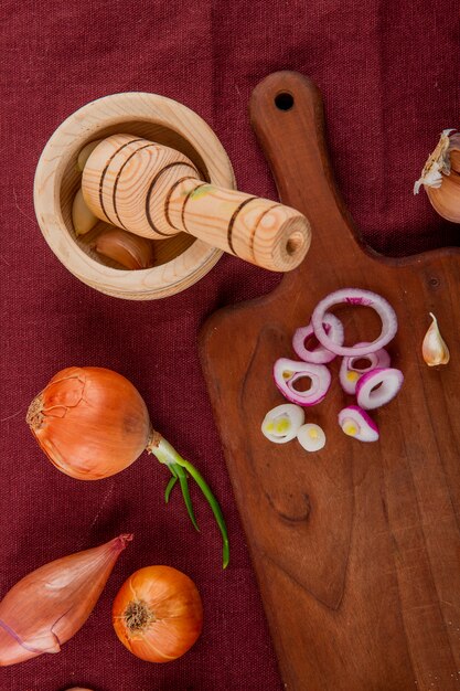 Top view of vegetables as whole and sliced onion on cutting board garlic in garlic crusher on burgundy background