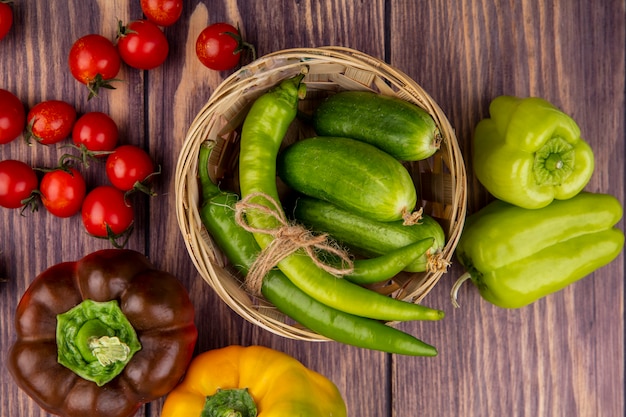 Top view of vegetables in basket as pepper and cucumber with tomatoes around on wooden surface