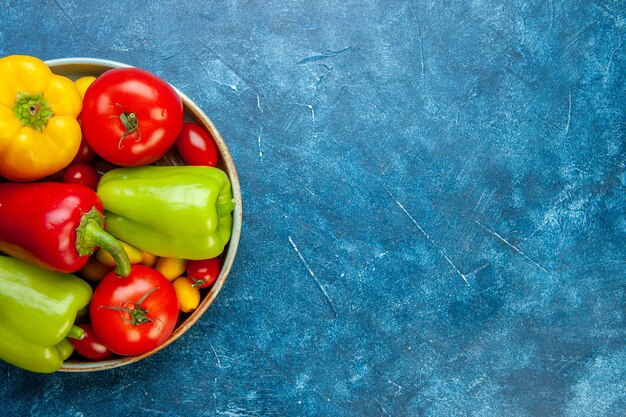 Top view vegetables cherry tomatoes cumcuat different colors bell peppers tomatoes on wooden platter on blue table with free space