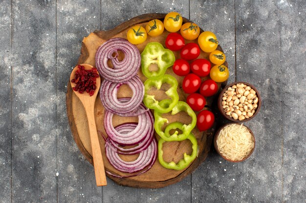 top view vegetables colorful sliced and whole onions green bell peppers tomatoes on the brown desk ad grey rustic floor