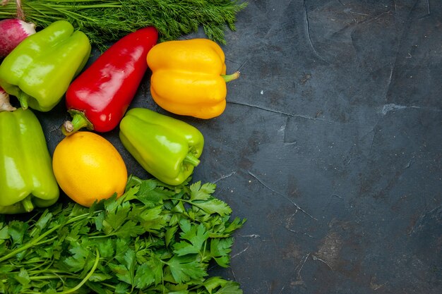 Top view vegetables different colors bell peppers lemon parsley dill on dark table with copy space