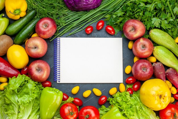 Top view vegetables and fruits lettuce tomatoes cucumber dill cherry tomatoes zucchini green onion parsley apple lemon kiwi notebook in center